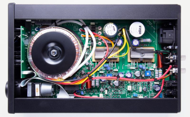 The io with its lid removed, showing the toroidal transformer, the two reservoir capacitors and one populated circuit board filling the case