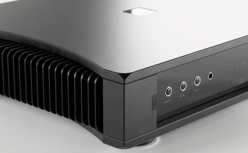 Macro of the Aethos front corner where the polished curved top meets the black heatsink fins, with the small fascia buttons behind