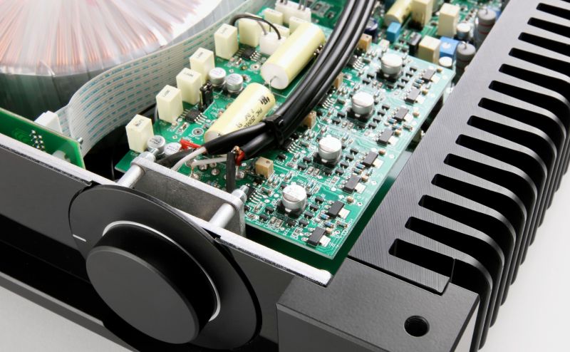 The Aethos with its lid off, seen past the volume knob: the populated circuit board, output transistors and the heatsink fins along the flank