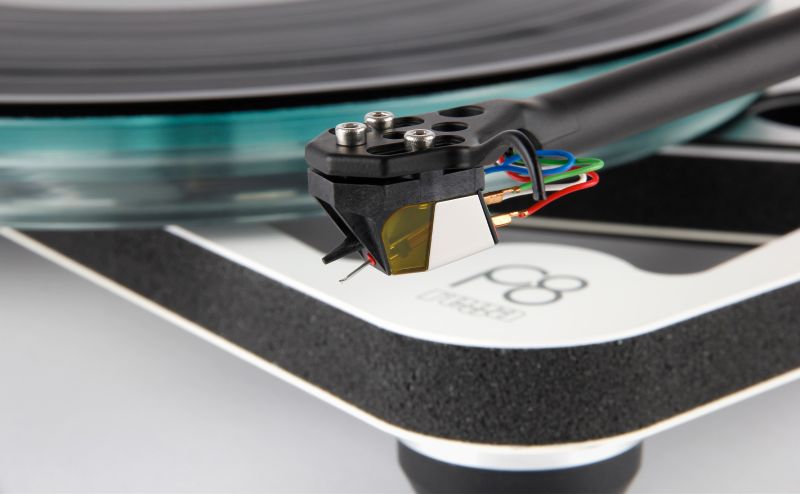 The Nd7 fitted to a Rega arm above a teal glass platter, the corner of a white and black plinth in view