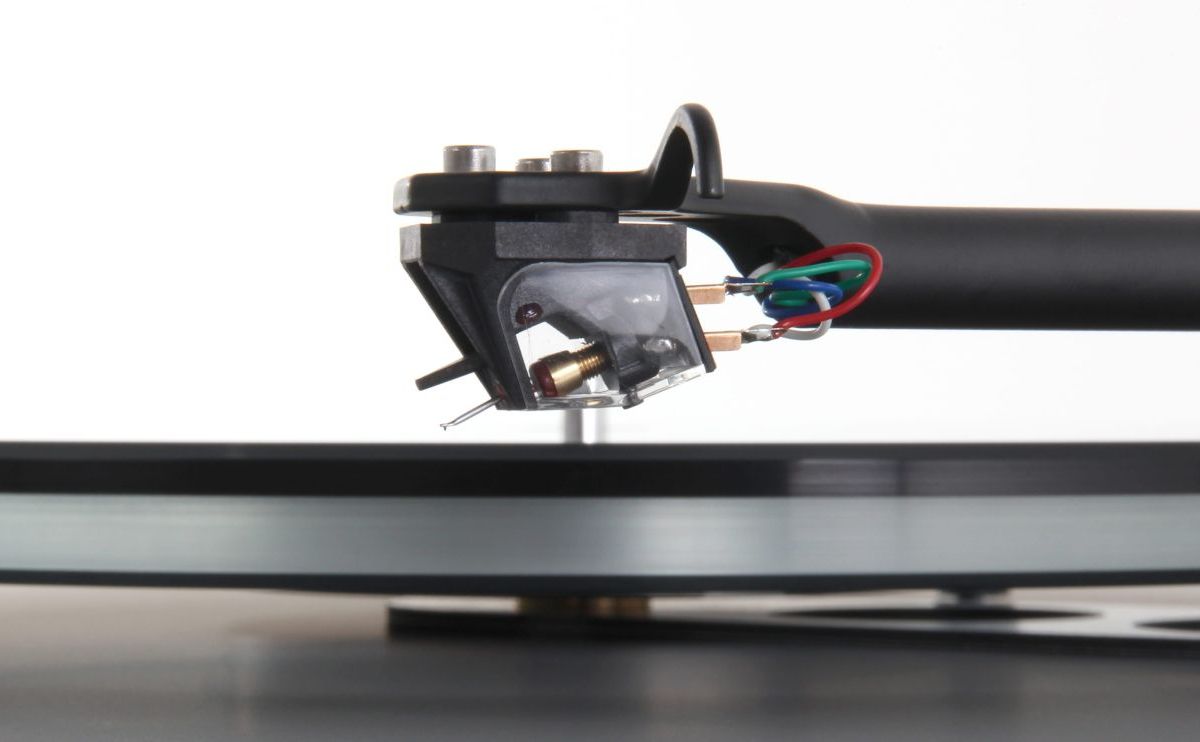 The Ania mounted on a Rega arm above a glass platter, headshell bolts and red, green, blue and white tag wires in view, the stylus just clear of the record surface