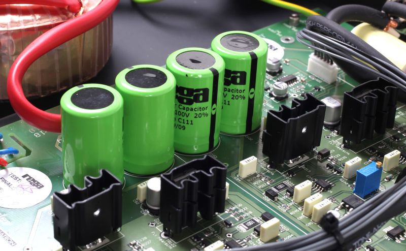 Macro of the Aura MC circuit board, with green audio grade capacitors, the red supply lead and the toroidal transformer behind