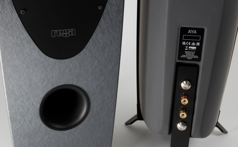 Close-up of the AYA's front port and rega badge in the cast GRC, with the rear panel's four binding posts and spiked foot alongside