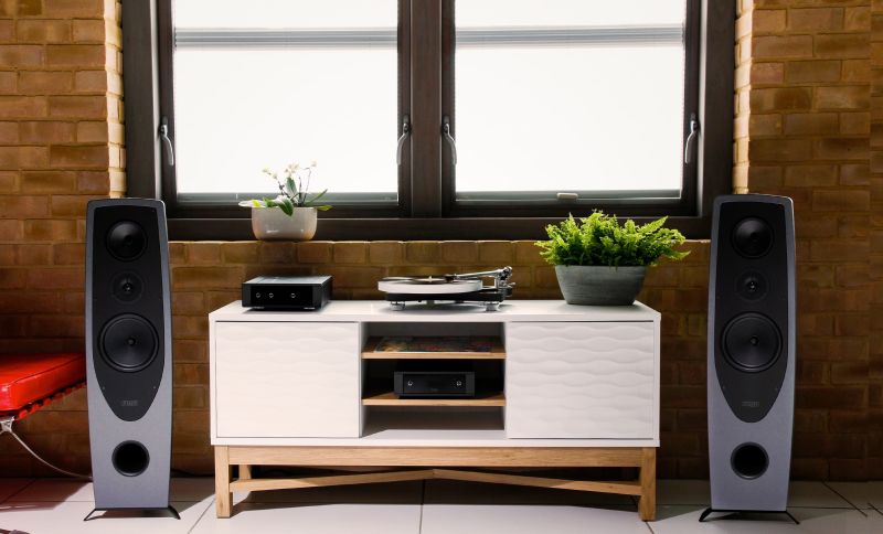 A pair of AYAs either side of a white sideboard carrying a Rega turntable, amplifier and CD player, in a brick-walled room
