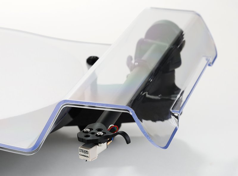 Detail of the clear dust cover of the Rega Replay, with the Carbon cartridge and the matt black tonearm beneath it.